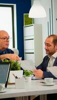 Senior businessman team leader brainstorming with colleague using paperwork showing ideas working in office. African woman using laptop in meeting broadroom, negotiations speaking with clients photo