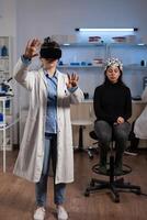 Neurologist doctor with virtual reality headset analyzing brain activity during neuroscience experiment in medical laboratory. Woman patient with eeg scanner having neurology disease photo