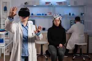 Neurologist specialist doctor with virtual reality headset analyzing brain evolution during neuroscience experiment in medical laboratory. Woman patient with eeg scanner having neurology disease photo