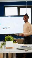 Black analyst using digital interactive whiteboard for presentation to a board of executives lawyers, in corporate meeting room, investors congratulating her clapping. Screen shows company growth data photo