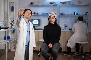 Woman patient wearing eeg scanner during neuroscience experiment in clinical neurology laboratory. Medical teeam of neurologist monitoring brain evolution analyzing nervous system activity photo