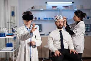 Physician doctor with virtual reality headset while neurologist woman adjusting eeg scanner of man patient analyzing brain evolution during neurology experiment. Scientist engineer using high tech photo