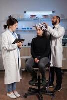 Scientist doctor explaining neurology disease symptoms to woman patient while neurologist researcher adjusting eeg headset during neuroscience experiment in lab. Specialist analyzing brain activity photo