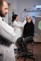 Neurologist doctor analyzing nervous system activity on monitor while specialist doctor adjusting eeg scanner of woman patient during neurology experiment. Medical team monitoring brain evolution photo