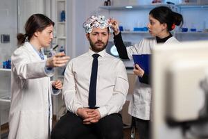 Medical team of scientists adjusting brain eeg analyzing nervous system evolution of man patient during medicine experiment in neuroscience laboratory. Physician doctor monitoring neurology activity photo