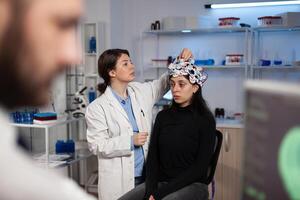 Neurologist researcher doctor adjusting eeg scanner on patient head analyzing brain evolution working at disease diagnosis during neurology experiment in high tech lab. Doctor explaining tomography photo