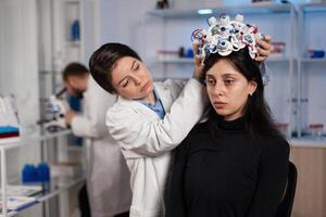 Scientist woman putting eeg headset on woman patient head during neurology experiment in medical laboratory. Neurologist doctor analyzing brain evolution monitoring nervous system activity photo
