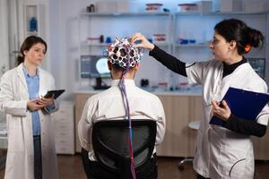 Medical team of neurologists adjusting brain eeg analyzing nervous system evolution of man patient during clinical experiment in neuroscience laboratory. Physician doctor monitoring neurology activity photo