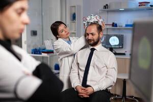 Specialist neurologist woman adjusting eeg headset analyzing brain activity of man patient monitoring nervous system information in medical laboratory. Physician doctor doing neurology experiment photo