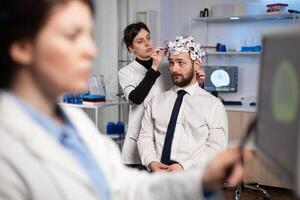 Specialist woman in neuroscience adjusting eeg headset analyzing brain activity of man patient monitoring nervous system evolution in medical laboratory. Physician doctor doing neurology experiment photo