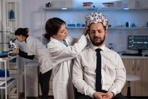 Specialist physician woman putting eeg headset on man patient monitoring brain evolution analyzing nervous system activity in clinical laboratory. Doctor in neuroscience doing medical tomography photo