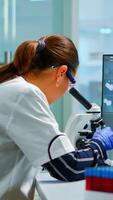 Biotechnology scientist researching in laboratory using microscope and typing on pc. Chemist examining virus evolution using high tech for scientific research of vaccine development against covid19 photo