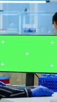 Woman researcher typing at computer with green screen mockup display, template in applied science laboratory. Engineer conducting experiments in background, examining vaccine evolution using high tech photo