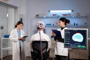 Man patient with eeg headset for brain scan standing in neurological laboratory during neurology experiment. Medical team of scientist monitoring brain activity analyzing nervous system photo
