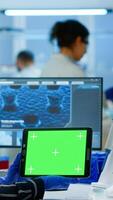 Medical research scientist working on tablet with green screen mock up template in applied science lab. Engineers conducting experiments in background, examining vaccine evolution using high tech photo