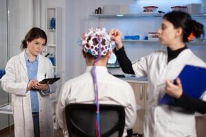 Man patient with eeg headset for activity scan standing in neurological laboratory during neurology experiment. Medical team of researcher monitoring nervous system analyzing brain evolution photo