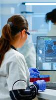 Laboratory doctor holding at blood sample and writing on computer while coworker opening door using digital computer with touch scan. Woman examining virus evolution using high tech and chemistry tools photo