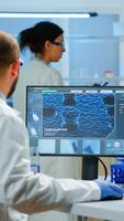 Man scientist working to develop a new vaccine in modern equipped laboratory, typing at computer. Group of biochemistry doctors examining virus evolution using high tech for researching treatment photo