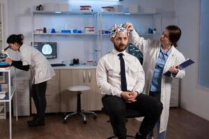Researcher neurologist woman adjusting eeg headset monitoring brain activity of man patient during medical experiment in modern laboratory. Scientist doctor analyzing nervous system. Medicine service photo