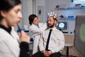 Specialist researcher woman putting eeg headset on man patient analyzing brain evolution monitoring nervous system activity in neurology laboratory. Doctor in neuroscience doing medical tomography photo