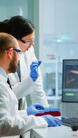 Team medical scientist conducting DNA experiments looking in computer holding test tube with blood sample working in science laboratory. Lab engineers in white coat analysing vaccine development photo