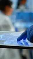 Close up of researcher using tablet, pointing, analysing DNA informations standing in medical laboratory. Viorolog doctor working to discover medical treatment, vaccine development, virus evolution photo