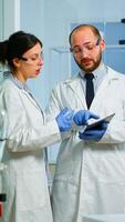 Chemist nurse explainig to doctor vaccine development in modern equipped laboratory pointing on tablet. Team of doctors examining virus evolution using high tech researching diagnosis photo