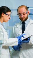 Scientist team meeting and discusssing treatment results standing in research laboratory pointing on tablet. Stuff examining vaccine development against covid19 virus using high tech for researching. photo