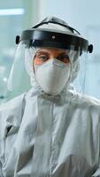 Tired microbiologist in coverall sitting in laboratory looking at camera. Team of scientits examining virus evolution using high tech and chemistry tools for scientific research, vaccine development. photo
