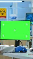 Scientist man wearing protection suit typing on computer with green mockup in modern equipped lab. Team of microbiologists doing vaccine research writing on device with chroma key, isolated display. photo