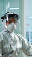 Tired laboratory doctor with overall suit working at computer and looking at camera. Scientist examining virus evolution using high tech, chemistry tools for scientific research, vaccine development photo