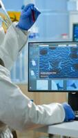 Back view of chemist man in coverall typing on computer analysing vaccine evolution in equipped laboratory. Team of doctors in ppe suit using high tech for researching treatment against covid19 virus photo