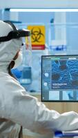 Scientist in protection suit typing on pc working in medical laboratory, writing on clipboard, developing inovative drugs against new virus. Doctor using high tech, chemistry tools for researching photo