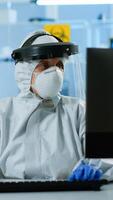 Laboratory technician assistant in ppe suit analyzing blood sample in test tube typing at pc. Doctor working with various bacteria, tissue, pharmaceutical research for antibiotics against covid19. photo