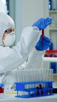 Researcher in coverall holding test tubes with blood sample for new treatment in medical laboratory. Team of doctors examining virus evolution using high tech for vaccine development against covid19 photo