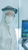 Tired doctor in protection suit against covid-19 looking exhausted at camera behind the glass wall working in danger area. Scientist examining virus evolution using high tech for scientific research photo