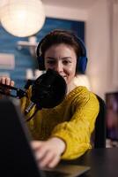 Portrait of social media vlogger wearing studio headset talking with online listeners using livestream microphone during podcasting at home in living room. Woman host recording production photo