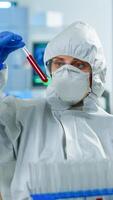 Neurologist with ppe suit working at vaccine development analysing blood sample in equipped laboratory typing on pc. Team examining virus evolution using high tech for research in treatment for covid19 photo