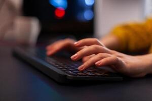 Closeup of gamer woman hand playing videogame during online gaming championship using RGB keyboard sitting at desk in streaming studio at home. Esport tournament. games competition photo