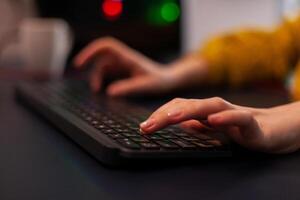 Closeup of player woman hand playing entertainment videogame during online streaming tournament using RGB keyboard sitting at desk in gaming studio at home. Esport championship photo