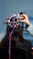 Woman patient wearing performant eeg headset scanning brain electrical activity in neurological research laboratory while medical researcher adjusting it, examining nervous system typing on tablet. photo