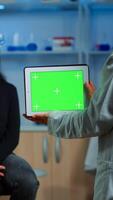 Neurologist doctor holding tablet with green screen in neurological research laboratory. Scientist using mockup chroma key display isolated desktop while patient with eeg headset wating in background photo