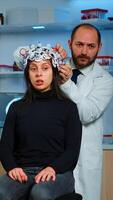 Professional neurological researcher explaning treatment result pointing on monitor while medical scientist adjusting eeg headset preparing for brain scan analysing electrical activity, nervous system photo