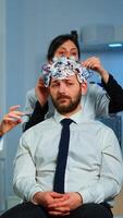 Neurological researchers explaning treatment result pointing on monitor while medical scientist adjusting brainwave scanning headset preparing for brain scan analysing electrical activity photo