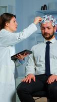 Man with brainwave scanning headset visiting professional doctor treating nervous system dysfunctions. Patient sitting in brain study laboratory while neurologist scientist adjusting eeg device photo