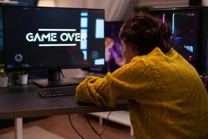 Angry streamer losing space shooter videogames during online entertainment competition at home in living room. Game over on computer screen. Player performing cybersport championship photo