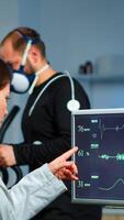 Muscular athlete with mask running on cross trainer in medical laboratory for monitoring his performance while ekg scan runs on computer screen and team of doctor researcher examining results photo