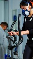 Woman athlete with mask running on cross trainer in sports science lab measuring performance and oxygen consumption during Vo2max test. Medical researcher looking at EKG scan monitoring heart rate photo