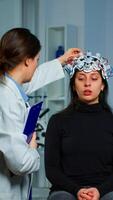 Neurological doctor cheking eeg headset explaining to patient diagnosis of disease and treatment for nervous system. Scientist researcher analysing brain scan and tomography on monitor in lab photo