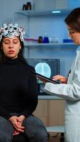 Researcher neurologist doctor asking patient's symptoms taking notes on tablet, adjusting high tech eeg headset. Doctor researcher controlling EEG headset analyzing brain functions and health status photo